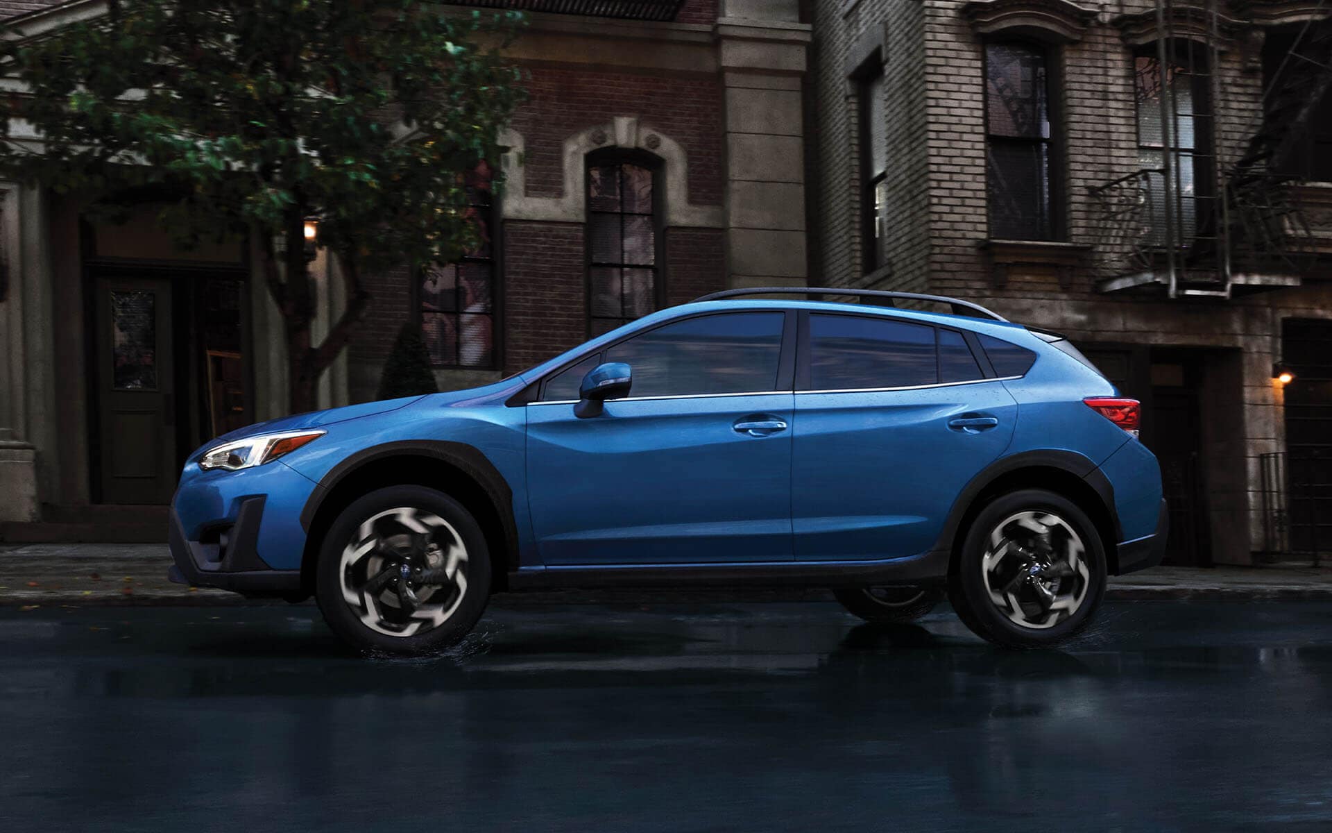 A blue Subaru Crosstrek parked on a city street in front of a brick building