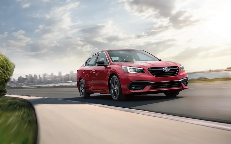 Front view of a red 2022 Subaru Legacy driving on a road heading out of a city
