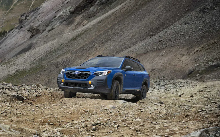 Front view of a blue 2022 Subaru Outback driving along rocky terrain