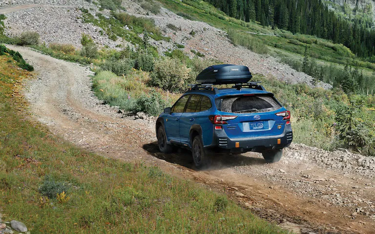 Back view of a blue 2022 Subaru Outback driving up rocky terrain