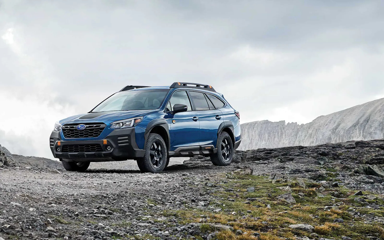 Side angled view of a blue Subaru Outback Wilderness parked on rocky terrain