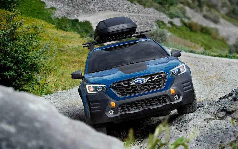 Front view of a blue 2022 Subaru Outback Wilderness driving up a rocky incline