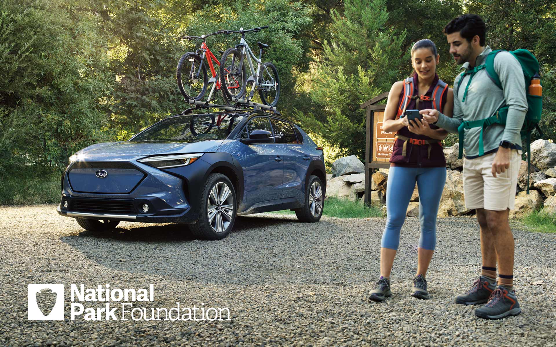 Couple getting ready for a hike next to their Subaru Solterra with bikes on the roof