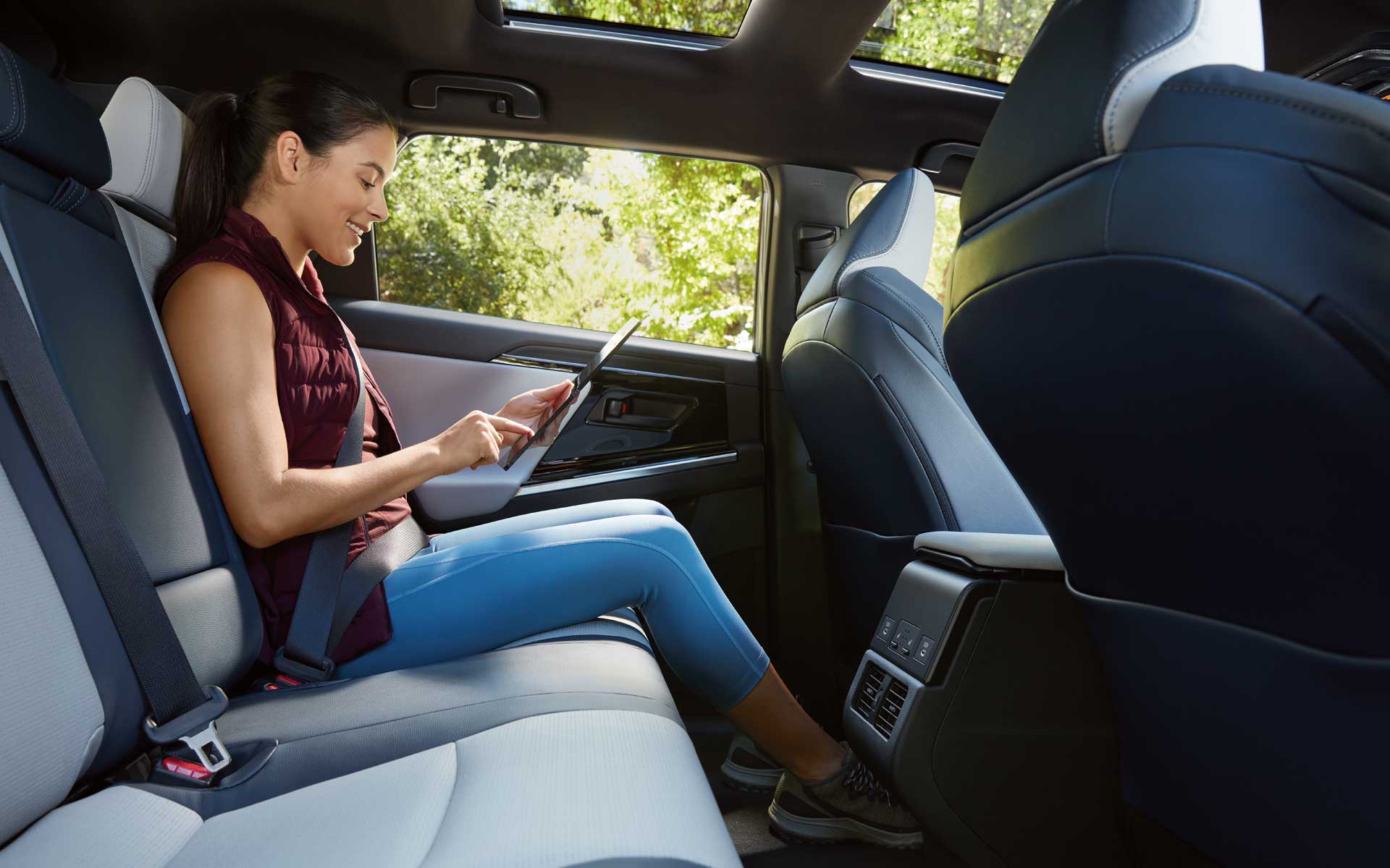 Side view of a woman using a tablet in the back seat of a Subaru Solterra EV