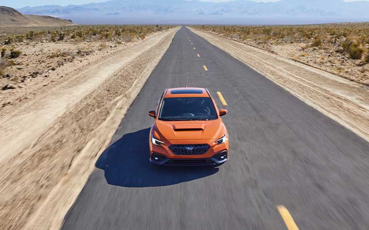 Front top view of an orange Subaru WRX driving down an open desert road