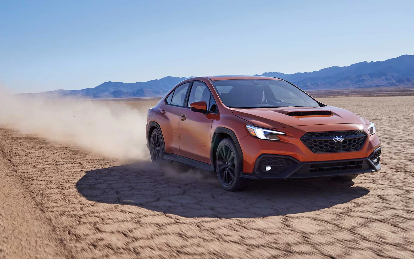 Front view of a man driving an orange Subaru WRX through the desert