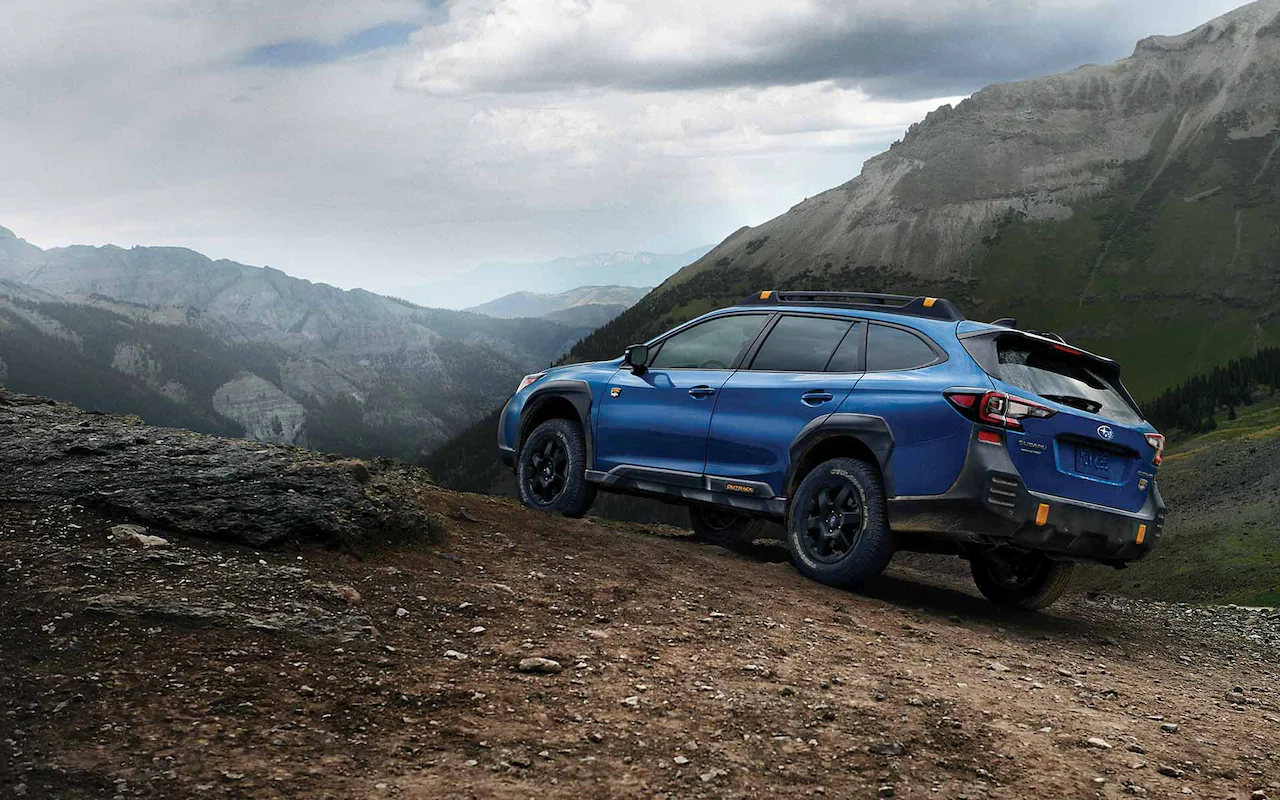 Side view of a blue 2022 Subaru Outback Wilderness driving up a dirt hill